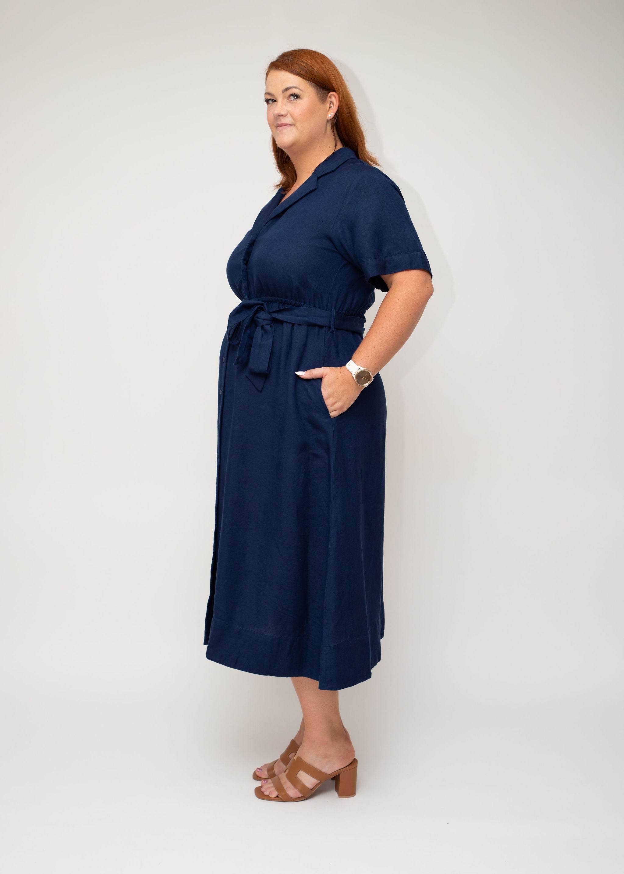 Side profile of the navy linen shirt dress, highlighting the cinched waist with a belt and flowing skirt for a relaxed yet structured look.