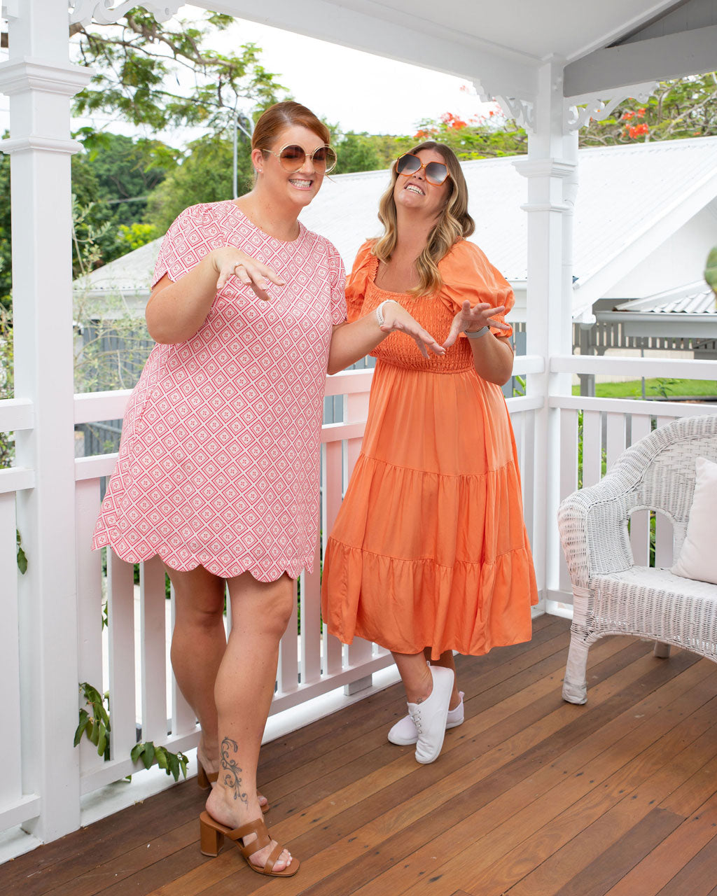 Two women laughing and posing on a porch while wearing vibrant, size-inclusive dresses from I Feel Pretty Boutique in Australia.