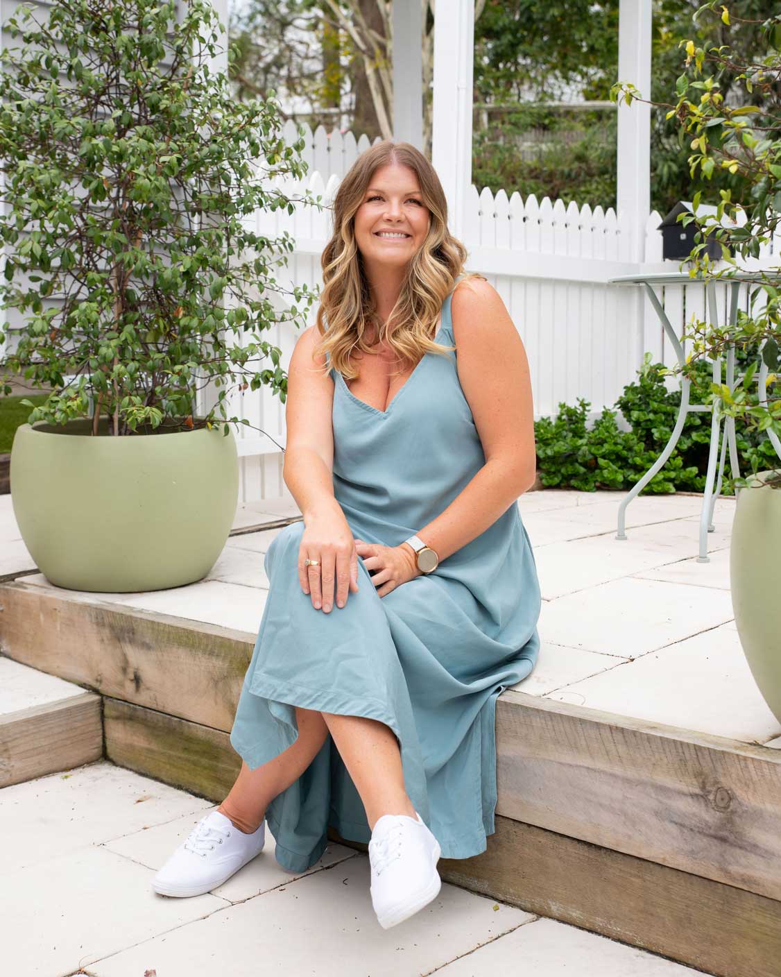 A woman wearing a flowing sage green dress, standing outdoors surrounded by greenery, embodying sustainable and stylish plus-size fashion by I Feel Pretty Boutique in Australia.